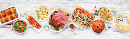 Traditional Easter ham dinner. Above view table scene on a white wood banner background. Ham, scalloped potatoes, vegetable side dishes, eggs, breads and lemon cake dessert.の写真素材