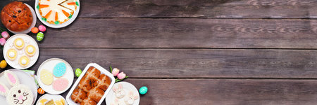Easter or spring dessert food corner border. Above view over a dark wood banner background. Bunny cake, colorful cookies, breads, tarts and and a variety of sweets. Copy space.の写真素材
