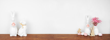 Modern Easter decor on a wooden shelf. Easter eggs, flowers, bunnies against a white wall banner background. Copy space.の写真素材