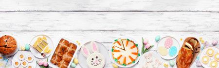 Easter or spring dessert food bottom border. Top view over a white wood banner background. Bunny cake, colorful cookies, breads, tarts and and a variety of sweets. Copy space.の写真素材