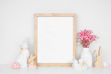 Modern Easter home decor shelf scene. Mock up portrait wood frame with Easter bunnies, eggs and pink flowers on a white shelf. Copy space.の写真素材