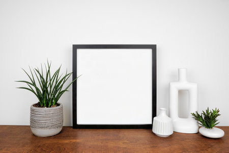 Mock up black square frame with potted plants and modern home decor. Wooden shelf against a white wall. Copy space.の写真素材
