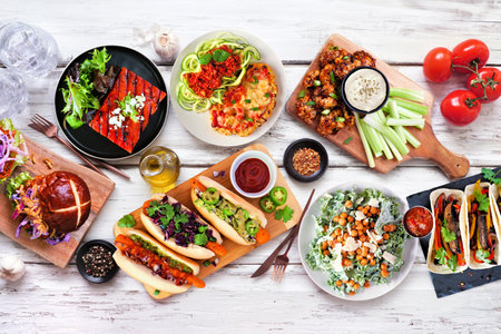 Healthy plant based vegetarian food table scene. Top down view on a white wood background. Jackfruit burger, mushroom tacos, watermelon and cauliflower steaks, carrot hot dogs, walnut bologneseの写真素材