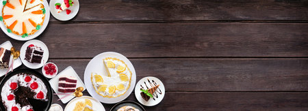 Dessert corner border with a variety of cakes. Above view over a dark wood banner background. Copy space. Black forest, lemon, carrot, red velvet, chocolate and cheesecakes.の写真素材