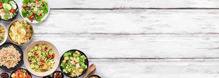 Variety of delicious homemade salads. Overhead view corner border on a white wood banner background. Summer food concept. Potato, caesar, pasta and green salads.の写真素材