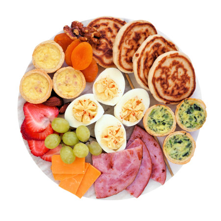 Breakfast or brunch grazing board. Selection of items including fruit, ham, quiche, pancakes and eggs. Top down view isolated on a white background.の写真素材