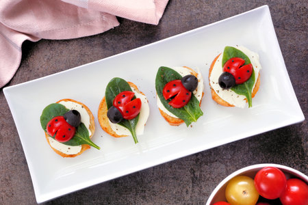 Fun summer theme ladybug crostini appetizers. Top view table scene against a white wood background. Top view.の写真素材