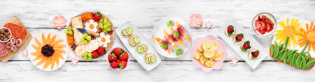 Summer garden party food table scene. Assortment of fun flower theme charcuterie items, cheese, fruit, vegetables and finger snacks. Above view on a white wood banner background.の写真素材
