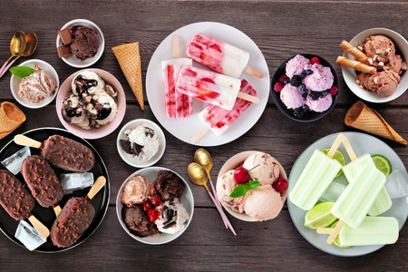 Cool summer food table scene. Variety of ice cream bowls, popsicles and frozen treats. Top view on a...