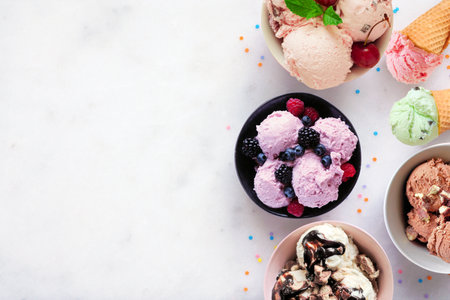 Summer ice cream side border. Bowls and cones of colorful assorted flavors. Top view on a white marble background. Copy space.の写真素材