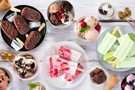 Cool summer food table scene. Assortment of ice cream bowls, popsicles and frozen treats. Overhead view on a white wood background.の写真素材
