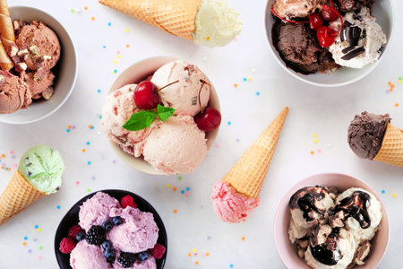 Summer ice cream table scene. Bowls and cones of colorful assorted flavors. Top view on a white marble background.の写真素材