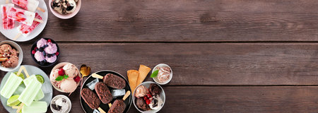 Cool summer food corner border. Variety of ice cream bowls, popsicles and frozen treats. Top view on a dark wood banner background. Copy space.の写真素材