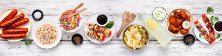 Summer BBQ food table scene over a white wood banner background. Assorted grilled meats, salads and sides. Top down view.の写真素材