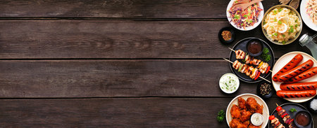 Summer BBQ food side border over a dark wood banner background. Assorted grilled meats, salads and sides. Top view.の写真素材