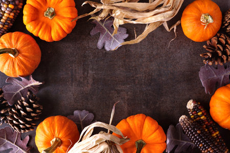 Autumn frame of pumpkins, corn, leaves and natural decor. Top down view on a dark stone background with copy space.の写真素材