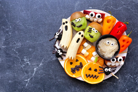 Healthy Halloween fruit and vegetable platter. Variety of fun, spooky treats. Above view over a dark stone background.の写真素材