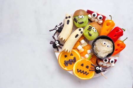 Healthy Halloween fruit and vegetable platter. Assortment of fun, spooky treats. Top view over a white marble background.の写真素材