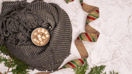 Cozy cup of hot chocolate with marshmallows wrapped in a winter scarf for the holidays