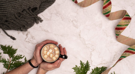 Female holding hot chocolate with marshmallows while wrapping presents on a marble background
