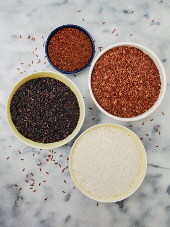 Ceramic bowls filled with a variety of grain and rice including red quinoa, red rice, black rice, and white rice on a marble top.の写真素材