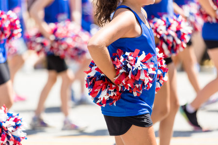 American cheerleader dressed in blue holding red, white, and blue pom poms on hips. Cheerleaders performing at a fourth of July parade.の写真素材