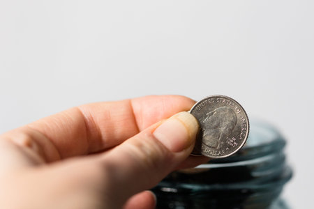 Close up of a hand putting coin into a glass jar on white background