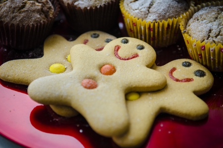 3 smiling happy gingerbread men with orange and yellow buttons on red metalic Christmas plate with muffinsの写真素材