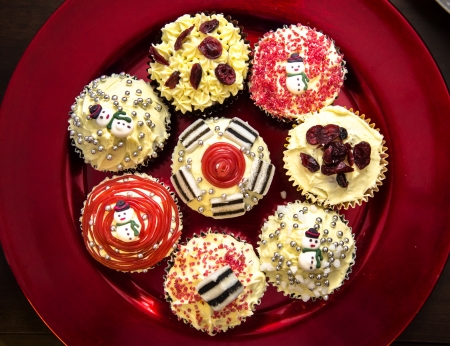 Christmas cupcakes with buttercream sweets, candy, liquorice and cranberries on metalic red plateの写真素材