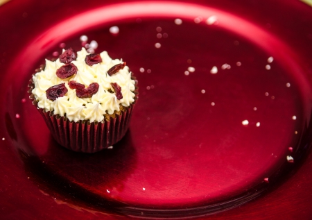 Christmas spiced muffin topped with buttercream and cranberries on a red metalic festive plate, the last one with crumbsの写真素材