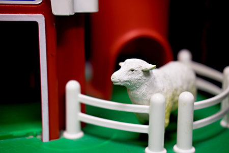 White toy sheep standing in front of red toy barnの写真素材