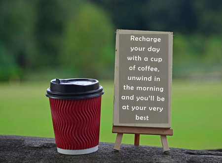 Red paper cup of coffee with text written on chalkboard and greenery background