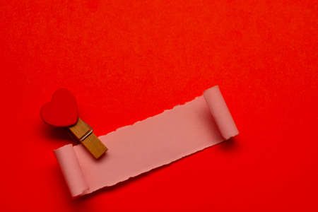 Torn paper and clothespin with heart shape on red paper background. Valentine's Day conceptの写真素材