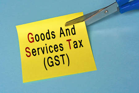 Scissors that cut yellow notepad with goods and services tax text on a blue background. Tax conceptの写真素材