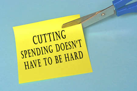 Scissors that cut yellow notepad with text on a blue background. Spending conceptの写真素材