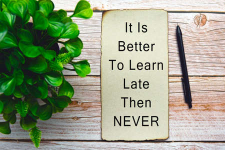 Motivational and inspirational quote on burnt edge paper with green plant on wooden desk - It is better to learn late then neverの写真素材