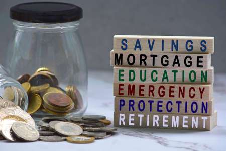 Text on wood block and glass jars with multicurrency coins - Savings, mortgage, educations, emergency, protection, retirementの写真素材