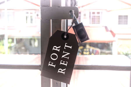 Text on tag and pad lock hanging on the window grill with blurred background of houses - For rentの写真素材