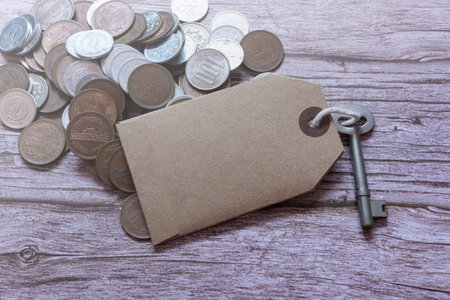 House key with brown tag and coins on wooden desk. For text use