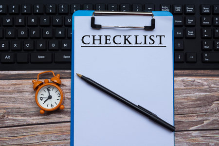 Text on blue clipboard on a keyboard with alarm clock and pen on wooden desk