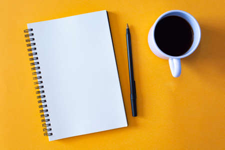 Notepad with pen and a cup of coffee on yellow background. For text useの写真素材