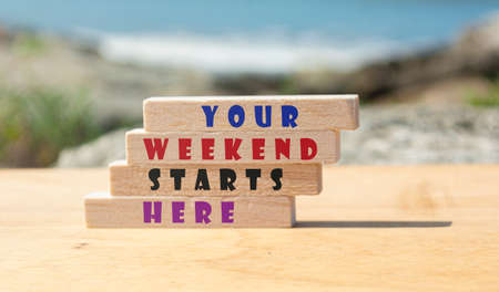 Motivational and inspirational quote on wooden block with blurred background of ocean - Your weekend starts hereの写真素材