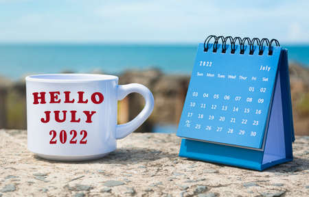 Hello July 2022 written on white coffee cup with blue calendar and background of ocean. New year time conceptの写真素材