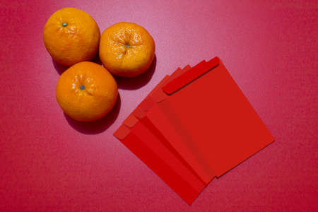Chinese New Year Concept - Mandarin oranges and red packet on red backgroundの写真素材