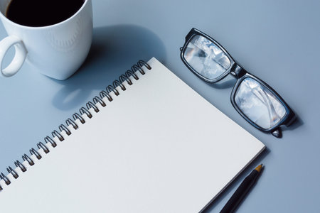 Notepad with coffee cup, glasses, pen on a desk. Directly above. Flat lay