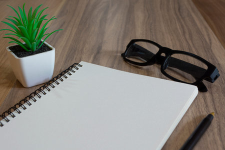 Notepad with glasses, pen and potted plant on wooden desk. Flat lay