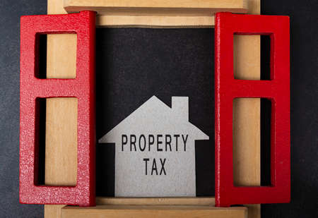 Property tax text on paper house model and in window frame on dark background. Real estate property tax and investment concept.の写真素材