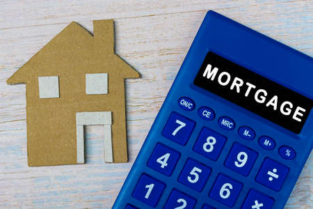 Mortgage text blue calculator and brown paper house model on wooden table. Housing loan conceptの写真素材