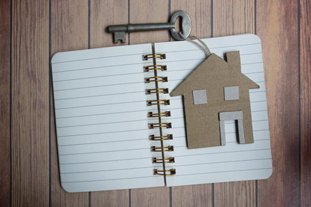 Notepad with house model and key on wooden desk. Directly above. Flat lay for text.
