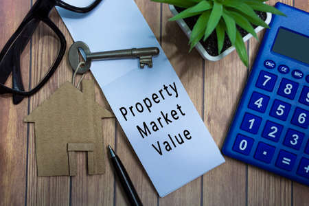 Property market value text on notepad with house model and key on wooden desk. Directly above. Flat lay, Property investment concept.の写真素材